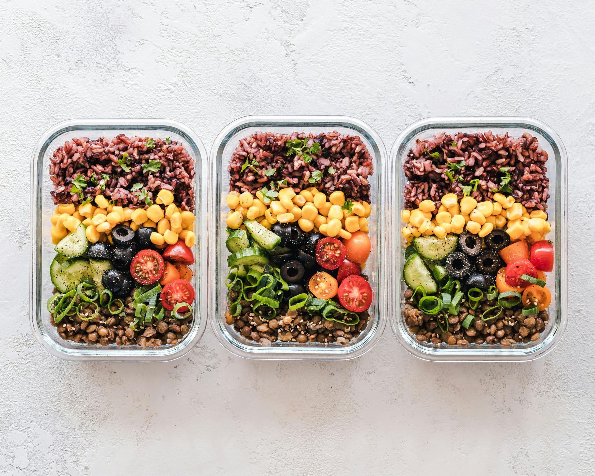 Tres recipientes de vidrio llenos de diferentes tipos de alimentos sobre una mesa.